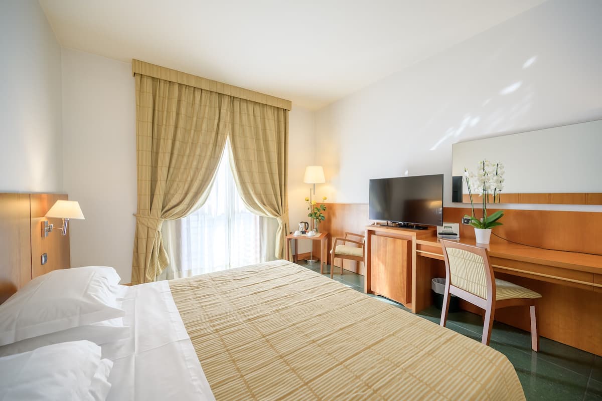 A hotel room with a bed, desk, television, and a potted plant.