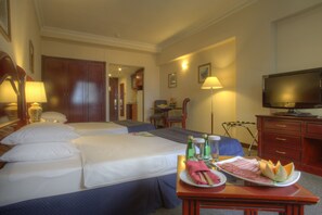 Habitación de hotel con dos camas, un televisor, una mesa de comedor con comida y un escritorio con una lámpara.