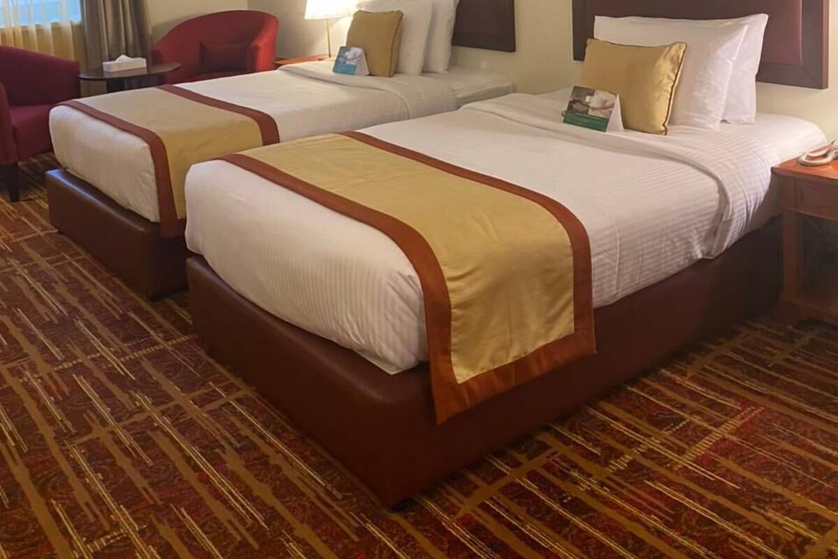 A hotel room with two beds, a red chair, a desk, and a lamp.