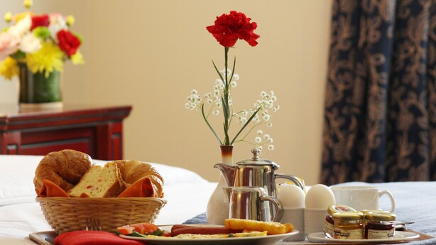 A breakfast setup with croissants, eggs, and honey on a tray, accompanied by a vase of flowers and a pitcher.