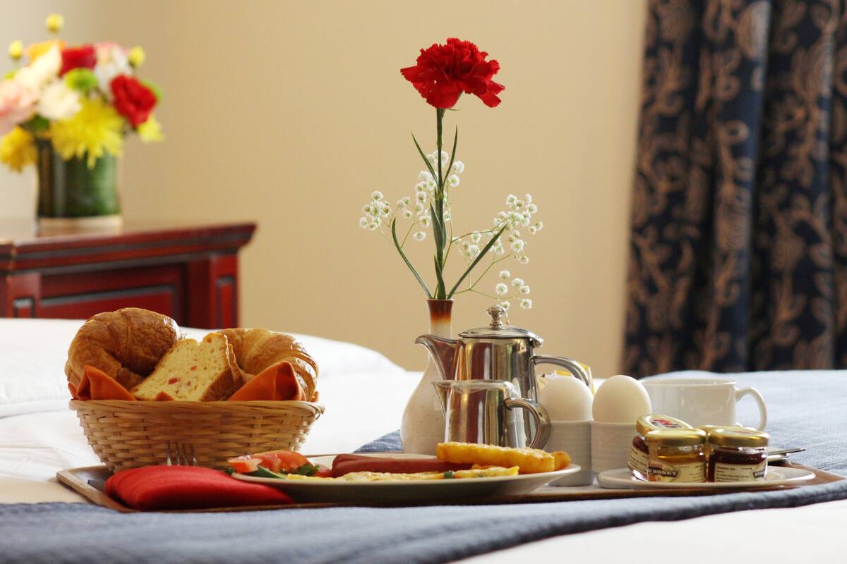 A breakfast setup with croissants, eggs, and honey on a tray, accompanied by a vase of flowers and a pitcher.
