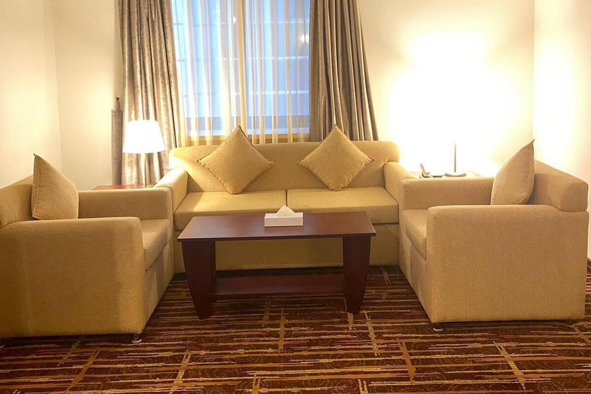 A hotel room with a sofa set, a coffee table, and a lamp.