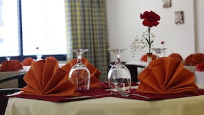 A table set with orange napkins, clear glassware, and a red rose in a vase.