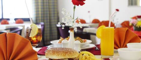A dining table with a meal consisting of a hamburger, fries, and a drink.