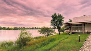 A lakeside property with a modern building, a grassy area, and a tree.