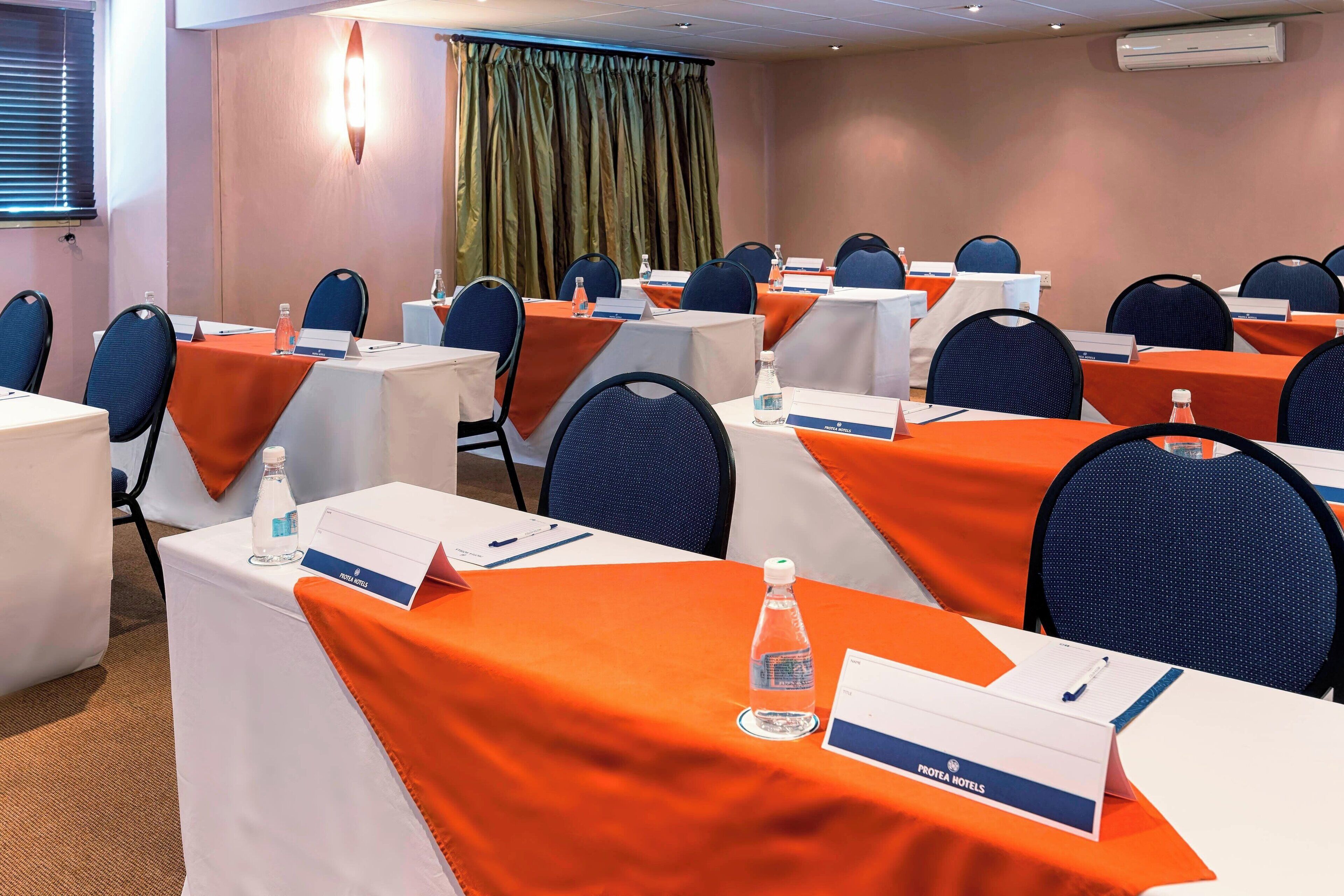 A conference room with tables covered in orange tablecloths, nameplates, and water bottles.