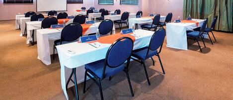 Une salle de conférence équipée de plusieurs tables et chaises, de plaques nominatives et d’un écran de projection.