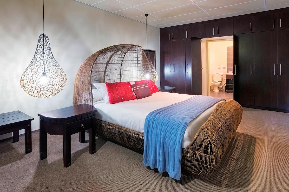 A bedroom with a bed, bedside tables, a hanging light fixture, and a wardrobe.