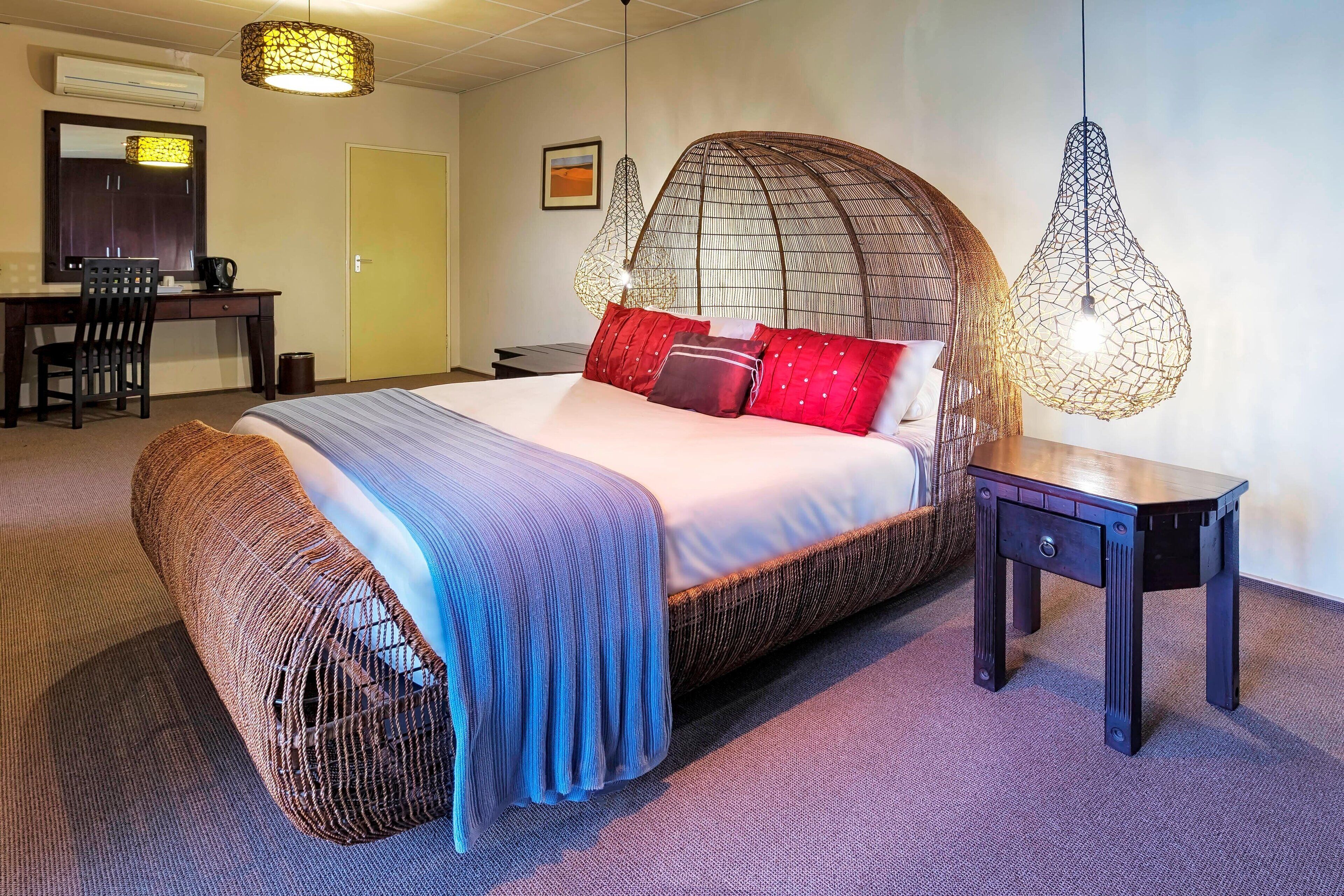 A bedroom with a large bed, a desk, and two hanging light fixtures.