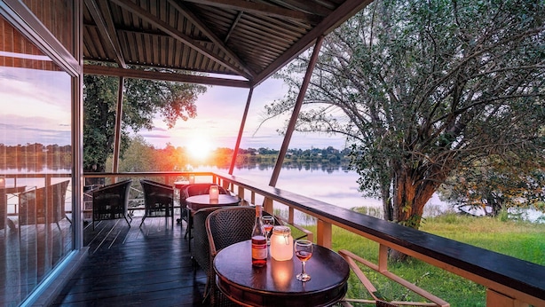 A wooden deck with outdoor seating, overlooking a lake and trees at sunset.