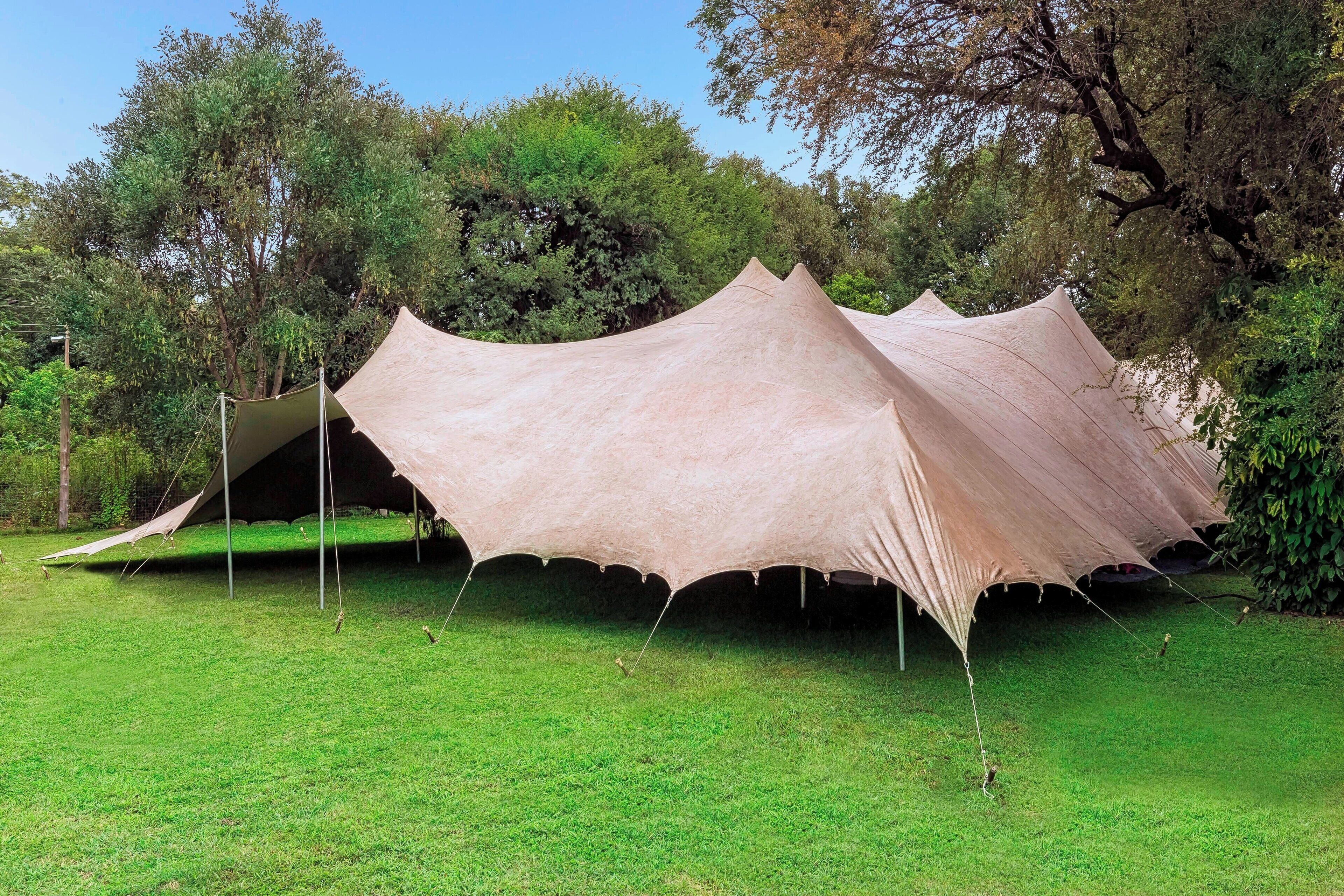 Una estructura grande y abierta, similar a una carpa, en un área con césped y árboles al fondo.