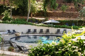 Relax by the serene pool surrounded by lush greenery and lounge chairs.