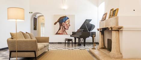 Una sala de estar con piso a cuadros, un sofá, una lámpara, un piano de cola y una chimenea.