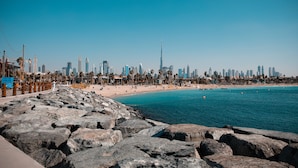 Un paysage urbain côtier avec un gratte-ciel imposant, une plage de sable et une côte rocheuse.