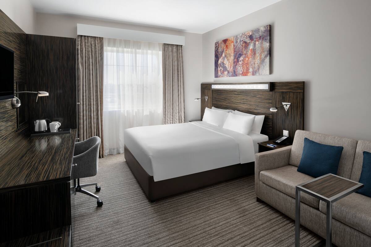 A modern hotel room with a large bed, a desk, a sofa, and a TV.