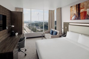 A hotel room with a large bed, a desk, a chair, a TV, and a view of the cityscape.