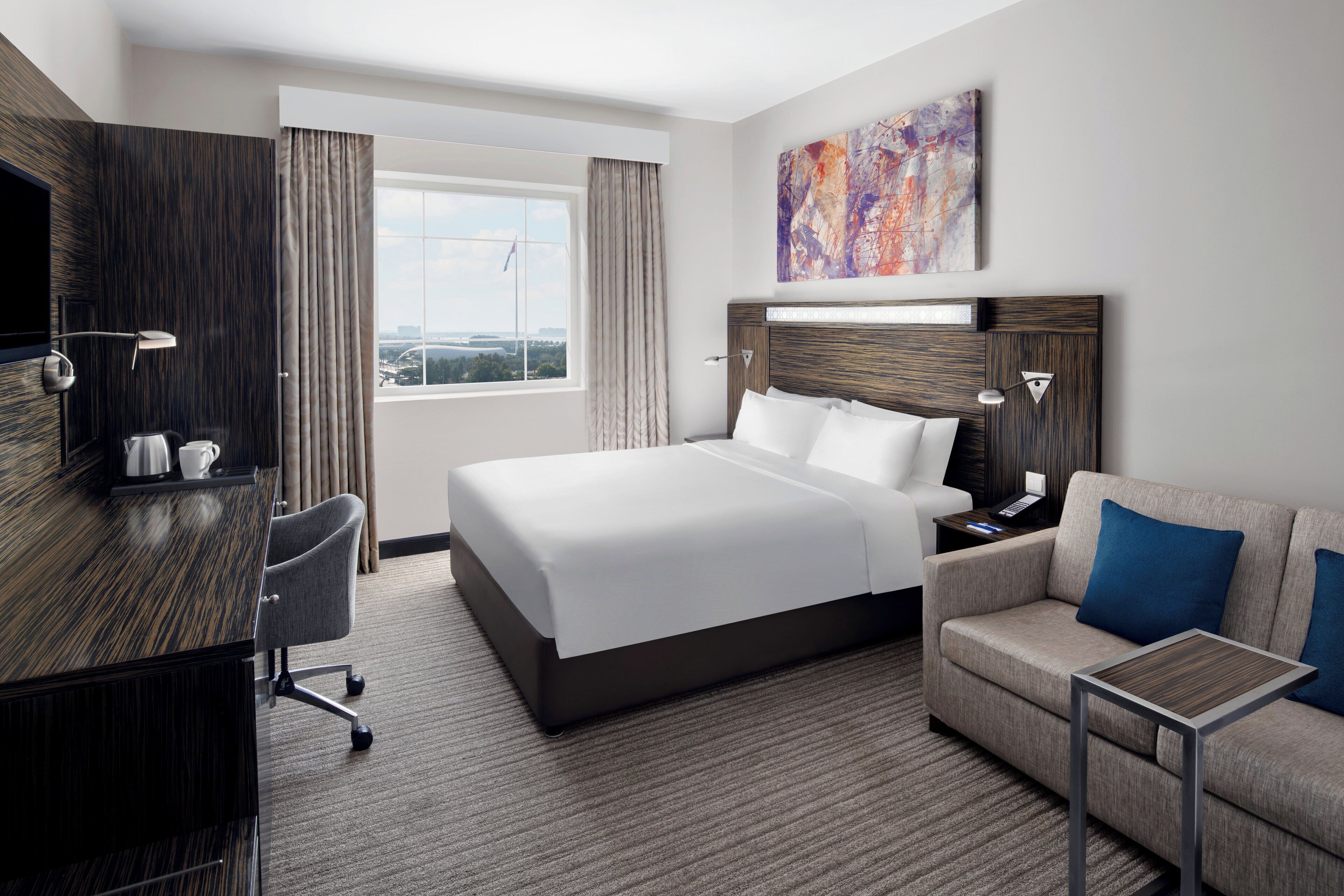 Quarto de hotel com cama, escrivaninha, cadeira, sofá, televisão e janela com vista.