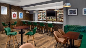 Un espace bar avec des tabourets verts, un comptoir en bois et un coin salon vert avec des sièges rembourrés.