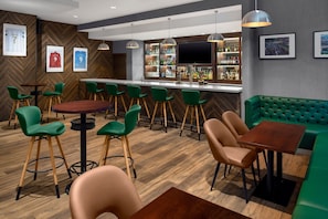 Uma área de bar com banquetas verdes, balcão de madeira e um espaço de estar acolchoado em tons de verde.