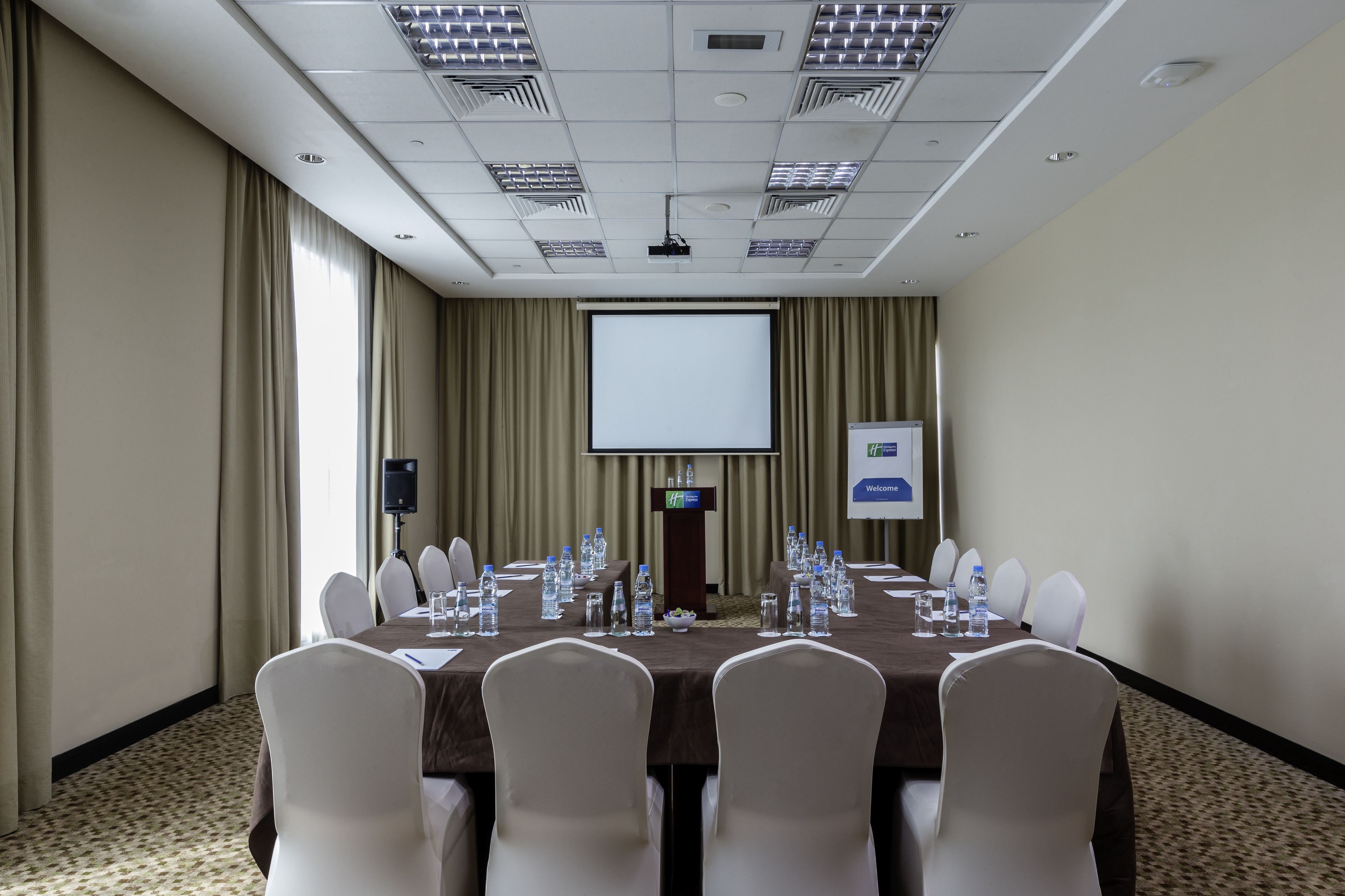 A conference room with a long table, white chairs, a projector screen, and a podium.
