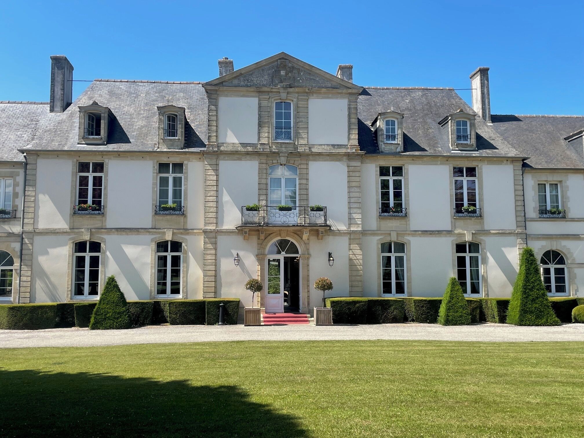 Un grand bâtiment historique à la façade symétrique, doté de nombreuses fenêtres et d’une entrée centrale surmontée d’un tapis rouge.