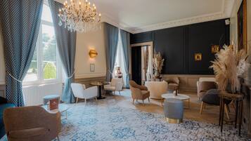 A spacious living room with a chandelier, patterned curtains, and a variety of seating options.