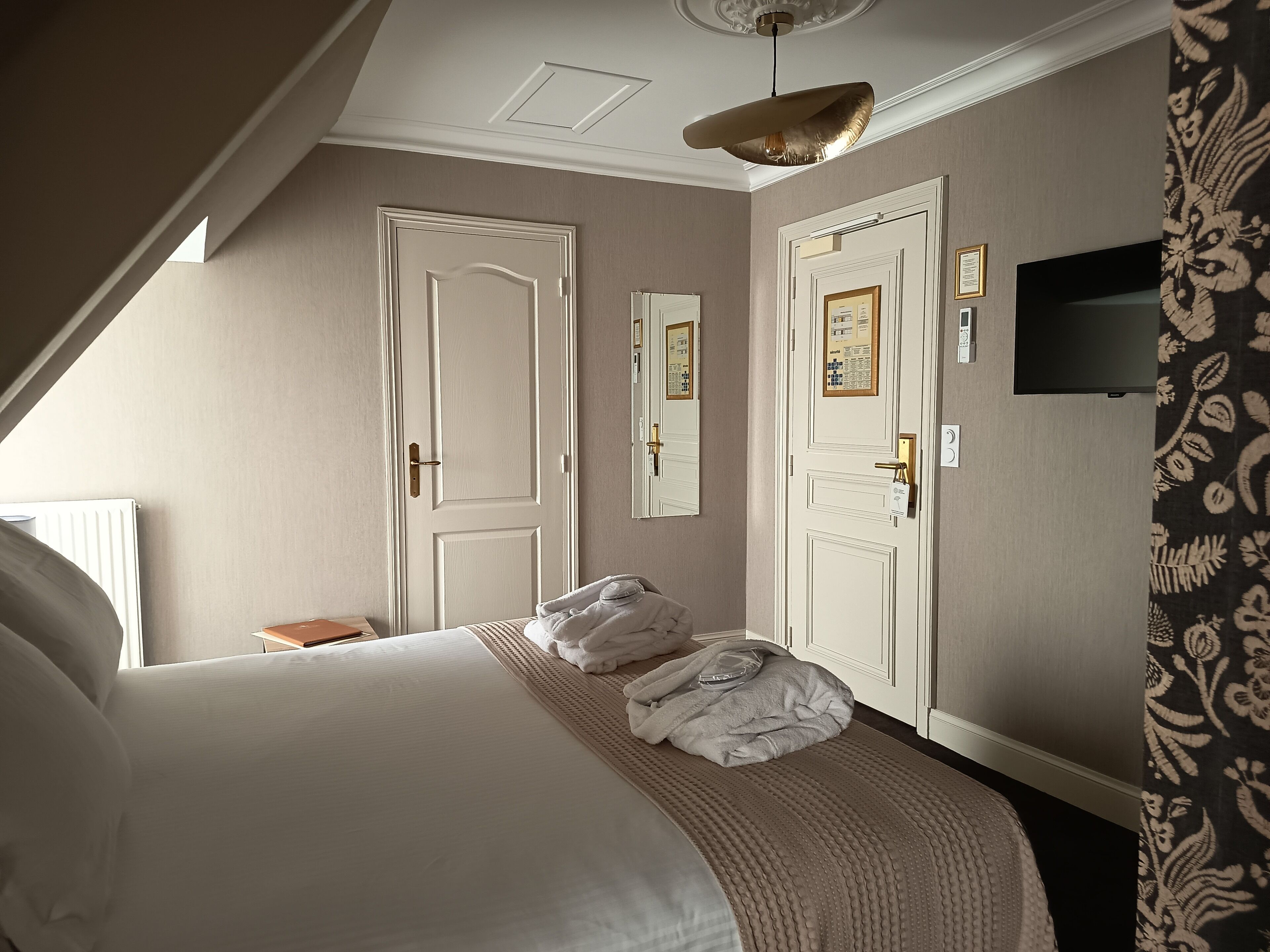 Hotellihuone, jossa on suuri sänky, kaksi ovea, kattovalaisin ja seinälle asennettu televisio.