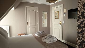 A hotel room with a large bed, two doors, a ceiling light, and a TV on the wall.