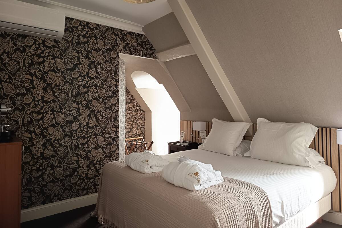 Hotellihuone, jossa on sänky, yöpöytä, lamppu ja koristeellinen seinä, jossa on kukallinen kuvio.