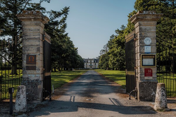 A gated entrance to a property with a formal stone gate, a clear pathway leading to a building, and a well-maintained lawn.