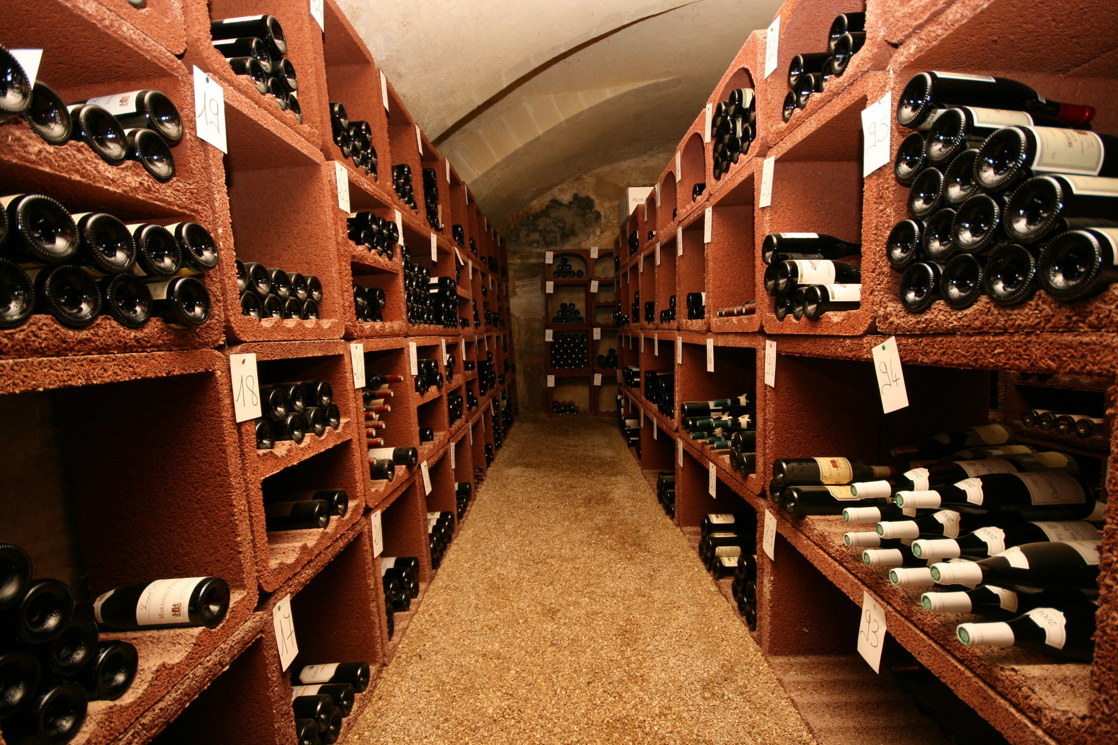Una bodega con hileras de botellas de vino en estantes, un pasillo estrecho y una pared de piedra.