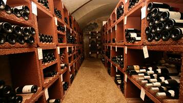 Una bodega con hileras de botellas de vino en estantes, un pasillo estrecho y una pared de piedra.