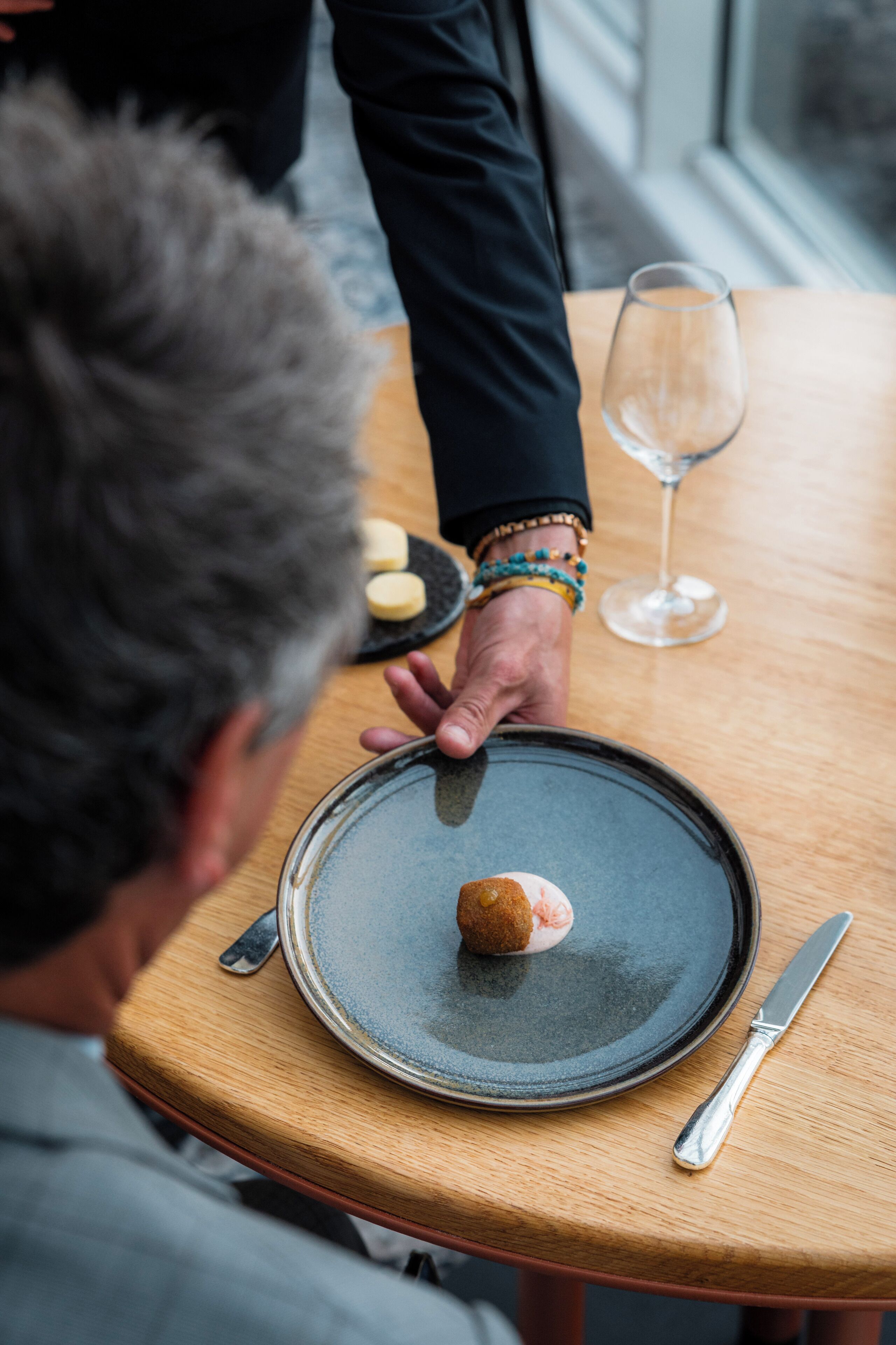 A person serving food on a plate with a knife and a glass on a wooden table.