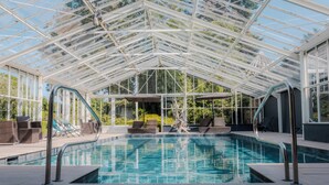 A glass-enclosed swimming pool with lounge chairs and a statue.