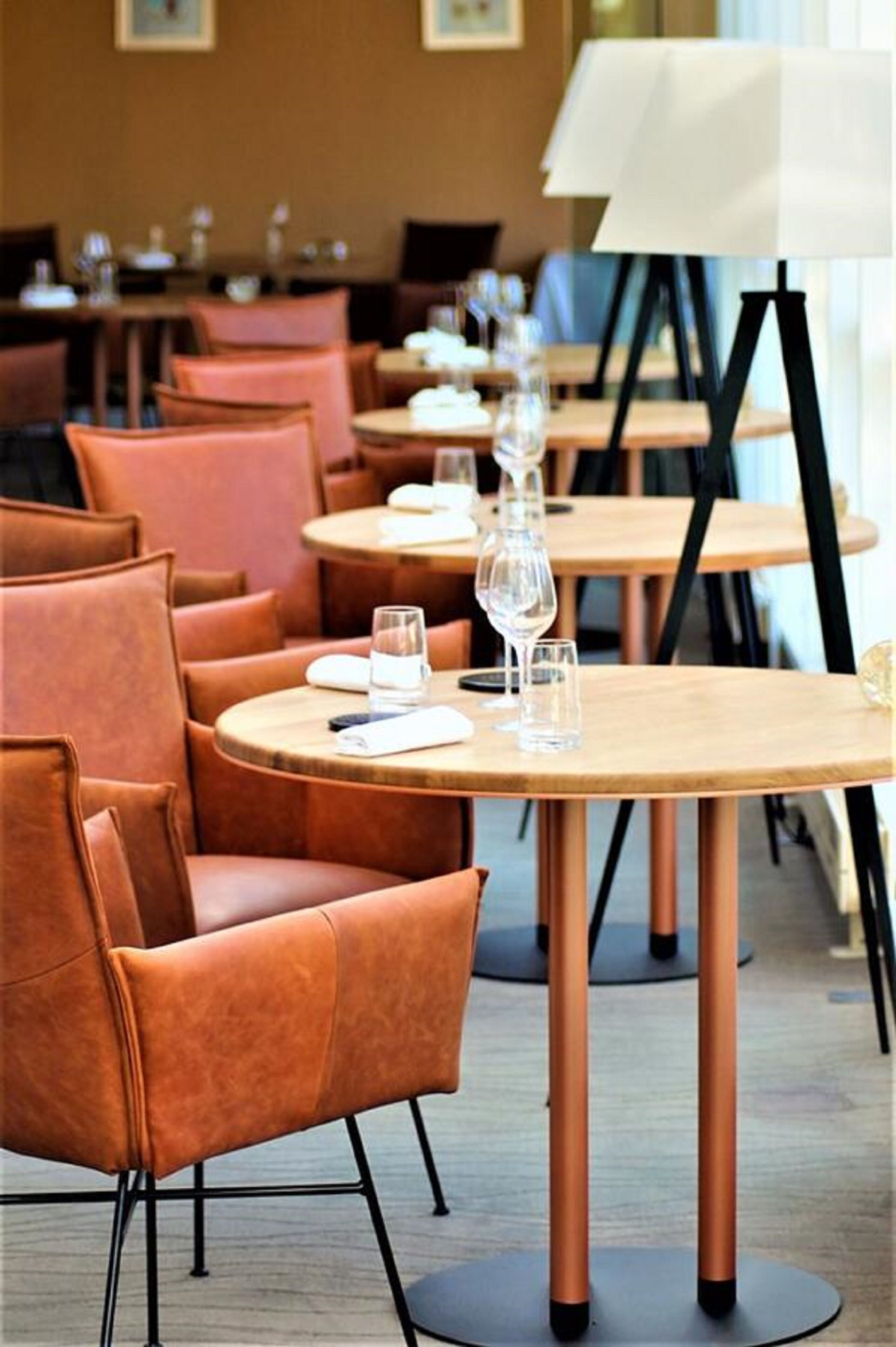 En restaurant med runde borde og orange stole, hvor hvert bord er dækket med et vinglas og et vandglas.