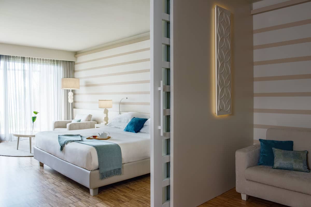 A modern hotel room with a large bed, bedside tables, and a seating area with a sofa.