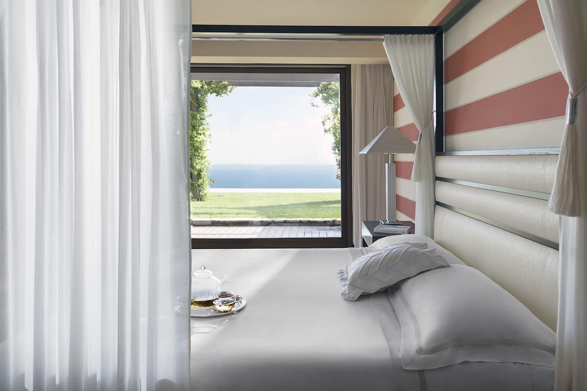 A bedroom with a large window, a bed, and a tea set on the bedside table.
