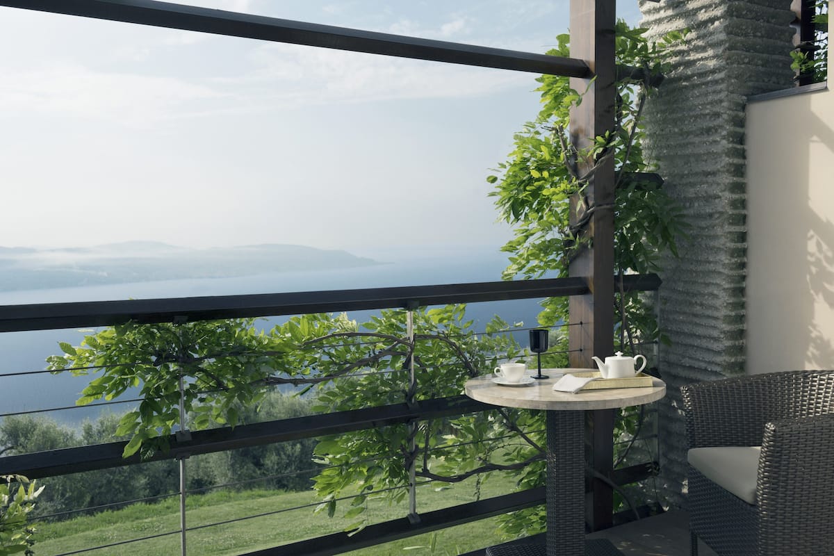 A balcony with a view of a lake, a wicker chair, and a small table with a teapot and cup.