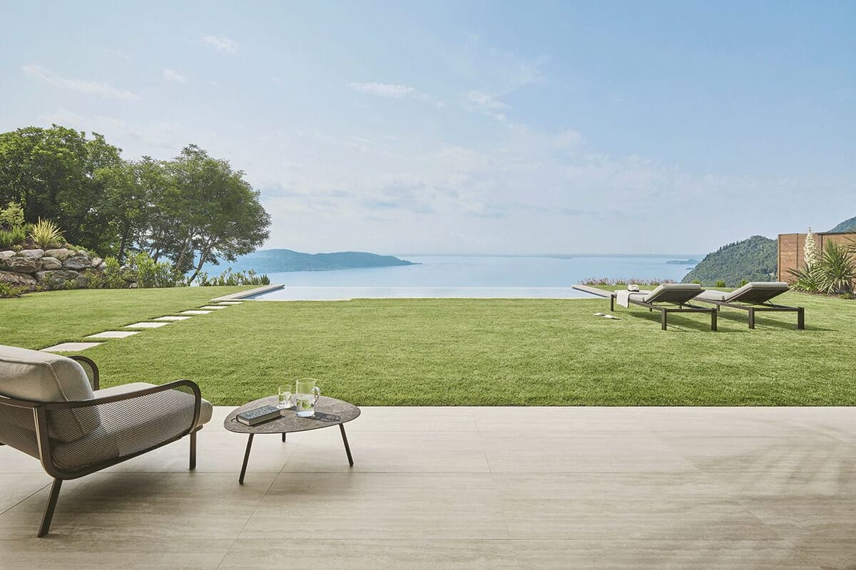 A patio with a view of the sea, a grassy lawn, and lounge chairs.