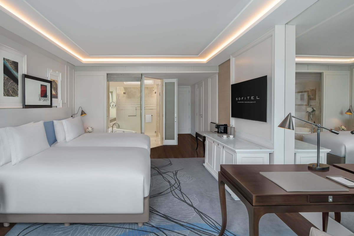 A hotel room with a bed, a desk, a chair, a coffee machine, and a mirror.