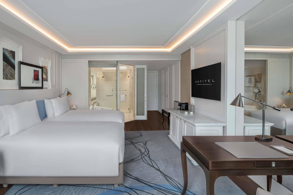 A modern hotel room with a large bed, a desk, and a bathroom visible through an open door.