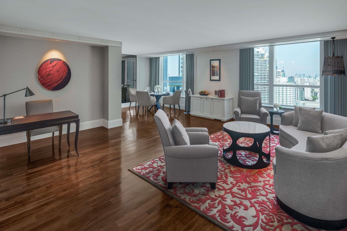 A modern living room with a dining area, a large window with a city view, and a red abstract painting on the wall.