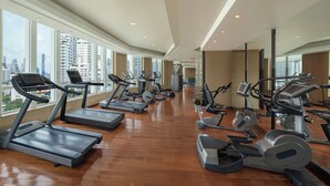 A modern gym with treadmills, elliptical machines, and stationary bikes. Large windows offer views of the cityscape. - Sofitel Bangkok Sukhumvit (Bangkok)