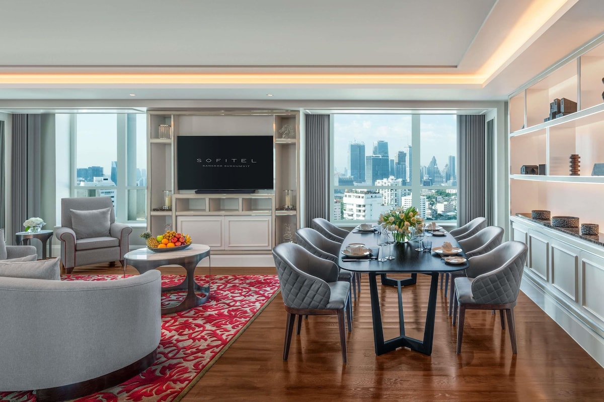 A modern living room with a dining area, a flat-screen TV, and a city view.