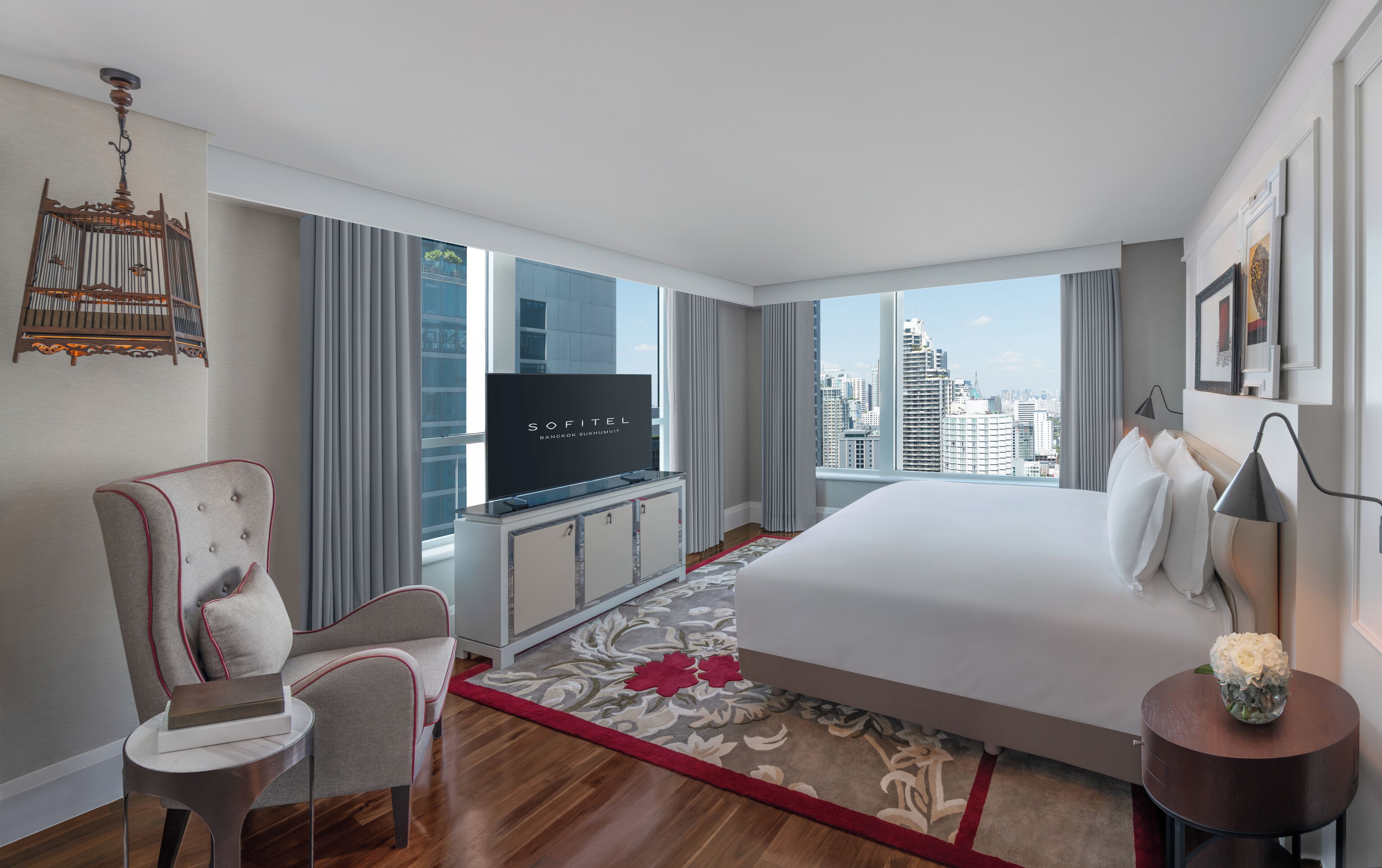 A hotel room with a large bed, a television, a chair, a desk, and a view of the cityscape.