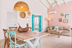 A dining area with a wooden table and chairs, a woven hanging light fixture, and a teal-colored door.