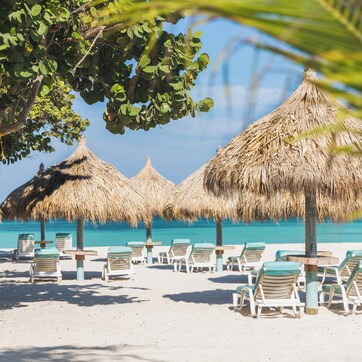 A beach with thatched umbrellas and lounge chairs.