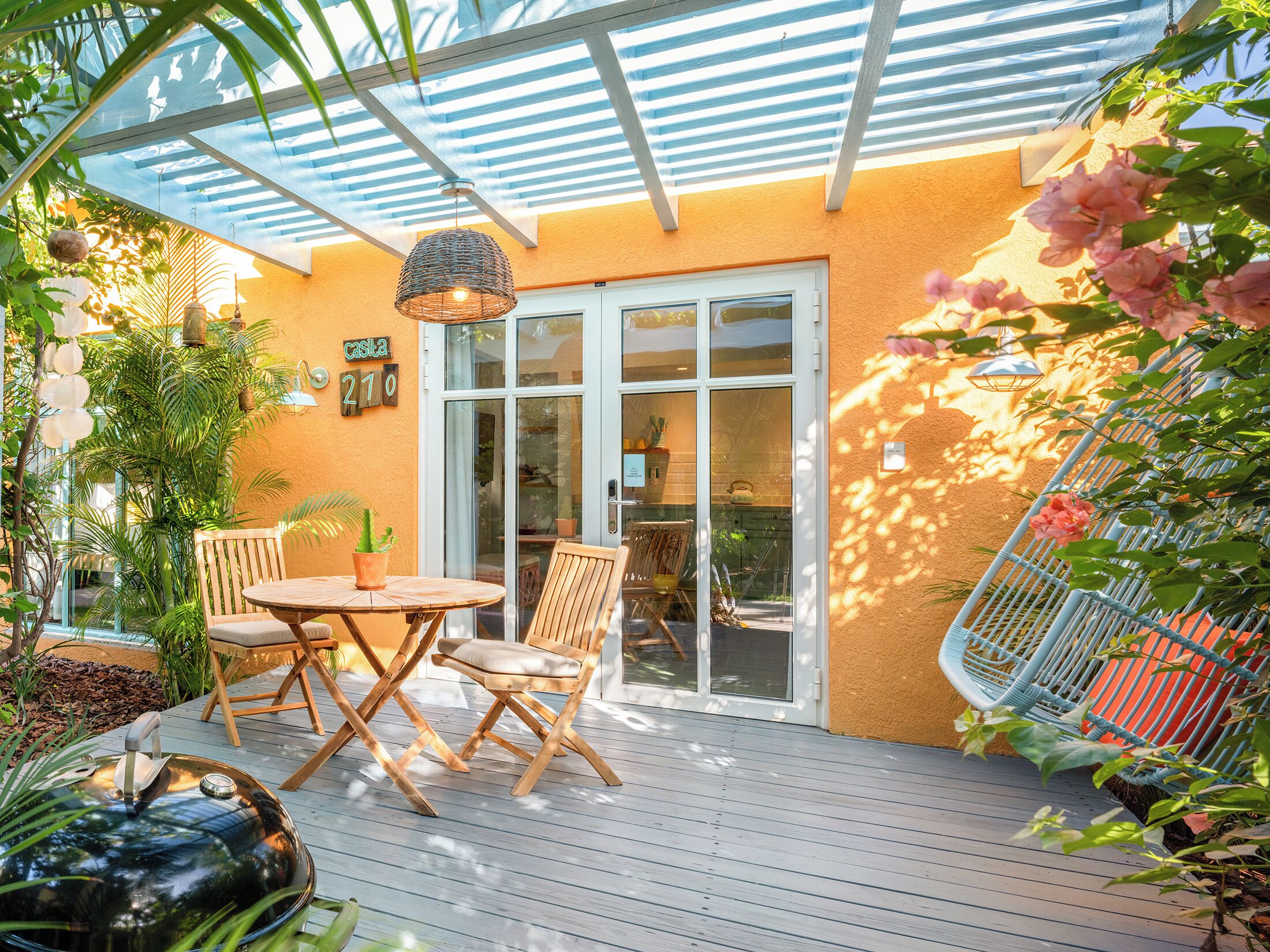 An outdoor patio with a wooden table and chairs, a hanging light fixture, and a covered area with a striped ceiling.