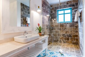 A bathroom with a stone shower wall, a white sink, and a blue-framed window.