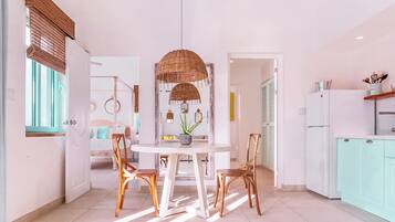 A bright kitchen with white cabinets, a dining table with wicker chairs, and a hanging light fixture.